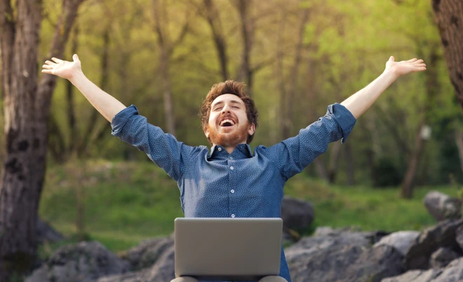 glücklicher Mann an Computer im Wald